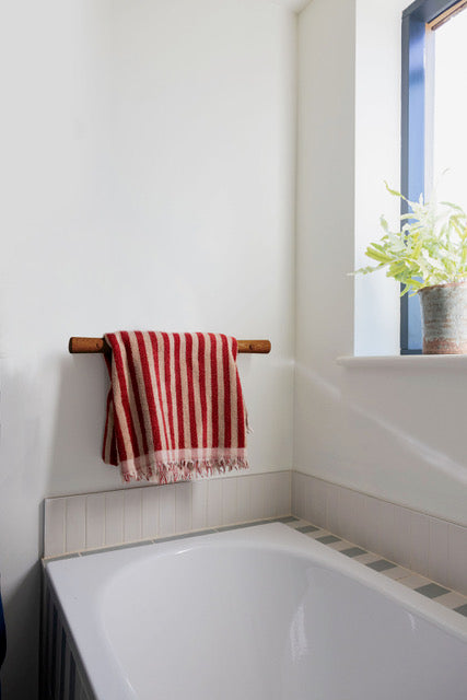 The Resilience Grab Rail in Iroko, holding a striped towel above a bath